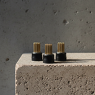 Three black cylindrical magnetic mini kenzans with gold spikes on a concrete surface.