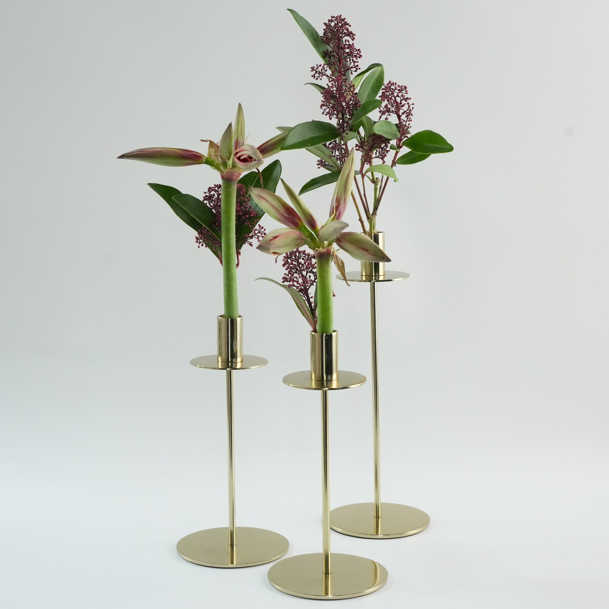 Magnetic mini kenzan in a et of three gold candle holders with amaryllis flowers on a light gray background