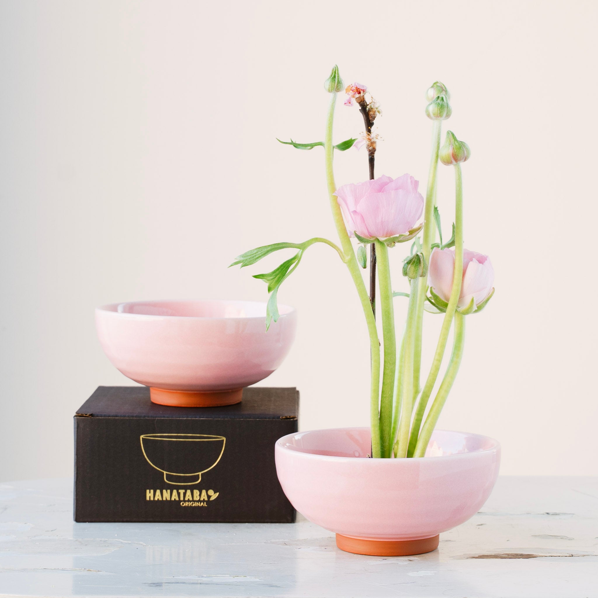 hanataba pink ceramic kenzan 'kobachi' bowl with flowers and a matching bowl on a white surface with a light background