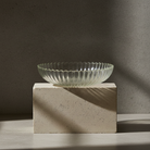 Clear rippled glass bowl on a concrete block with a dark background