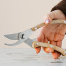 Hand holding a pair of hanataba garden shears with wooden handles on a light background