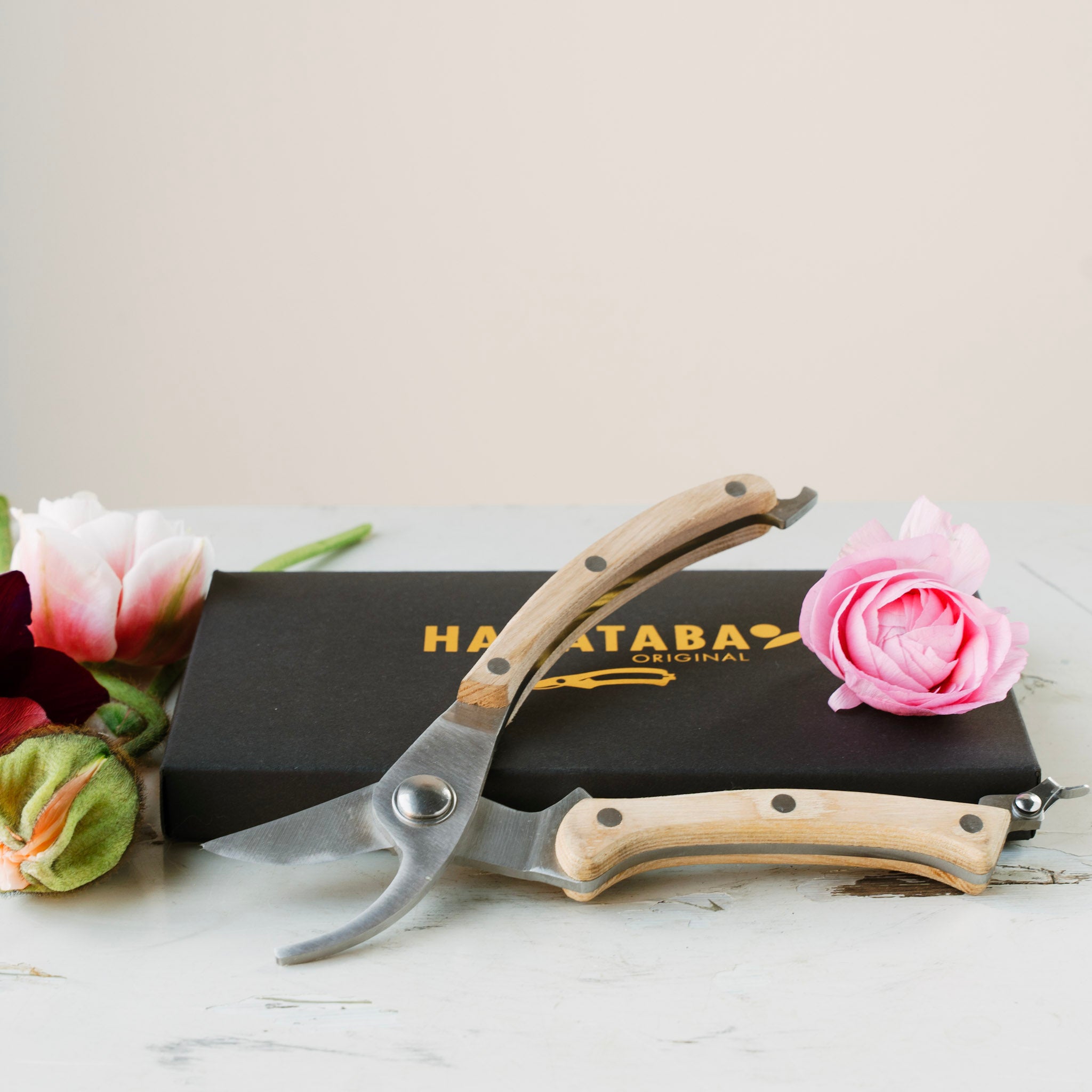 Hanataba Garden shears with wooden handles on a white surface with flowers and a black box.