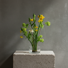 Glass vase with yellow and green flowers on a hanataba kenzan 70 mm standing on a concrete block against a gray background