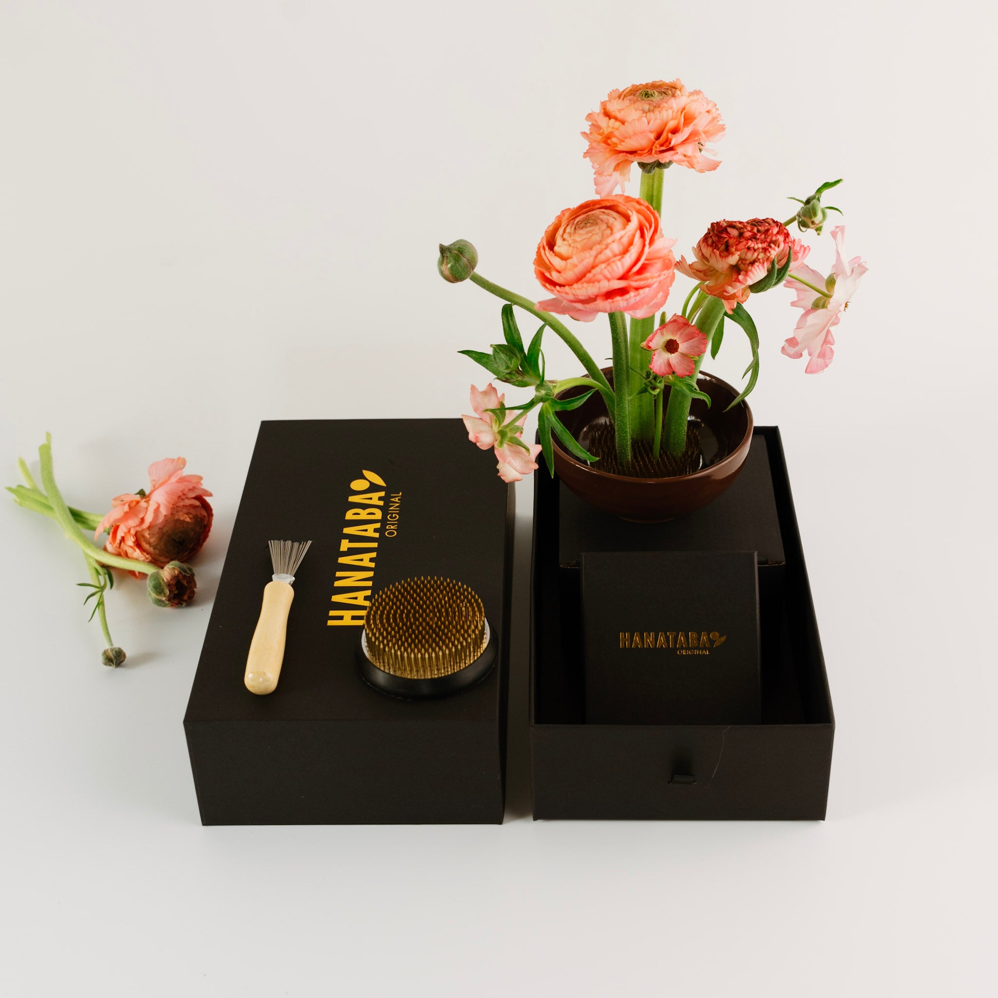 Floral arrangement in a black box with 'HANATABA' branding, including a brush and other items.