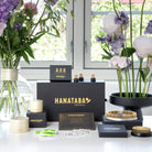 Hanataba bouquet twister champagne gold, kenzan 70 mm, magnetic mini kenzan and kenzan ring 120 mm alongside with water pearls and fresh cut flower nutrition product display with flowers and packaging on a table.