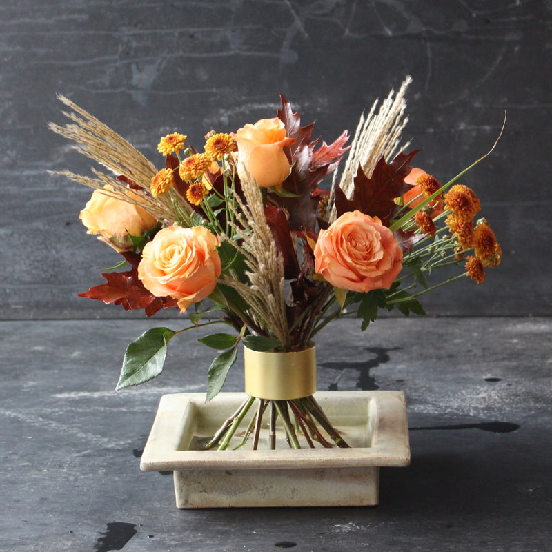 Autumn-inspired bouquet with orange roses and seasonal foliage, neatly bound by a Hanataba Bouquet Twister in champagne gold.