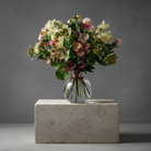 Bouquet of fresh pink and white flowers arranged in a globe shaped glass vase filled with water. The "Hanataba Bubble Glass Vase" also contains a "Hanataba Bouquet Twister" in the pink champagne color. The glass vase is placed in a white background next to a black packaging box with the Hanataba logo printed in gold.