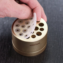A hand inserting a white silicone disc into a champagne gold Hanataba flower holder, showcasing the device's innovative design