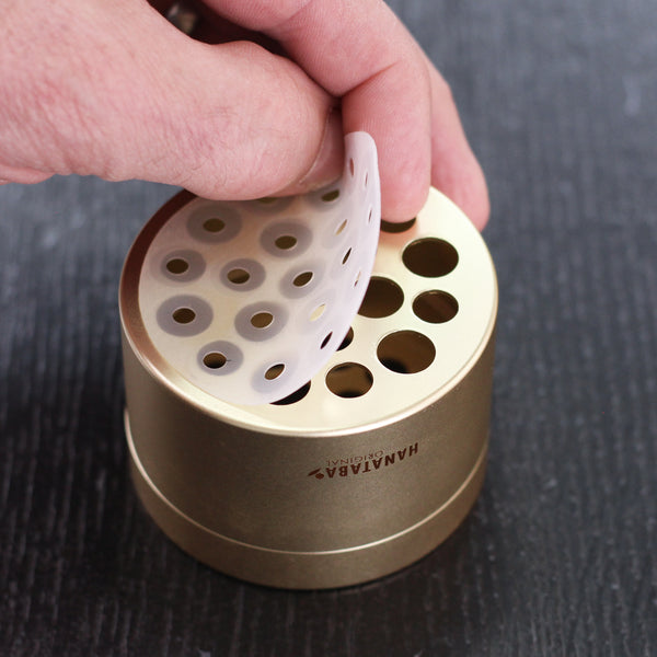 A hand inserting a white silicone disc into a champagne gold Hanataba flower holder, showcasing the device's innovative design
