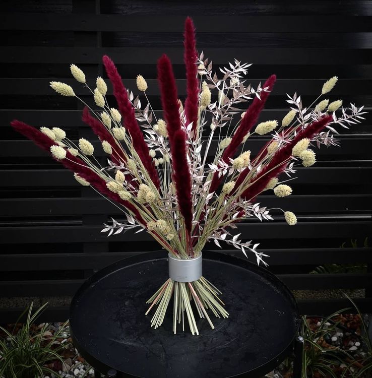 A vibrant ikebana arrangement of crimson and cream dried flowers in a Hanataba bouquet twister, set against a black slatted backdrop