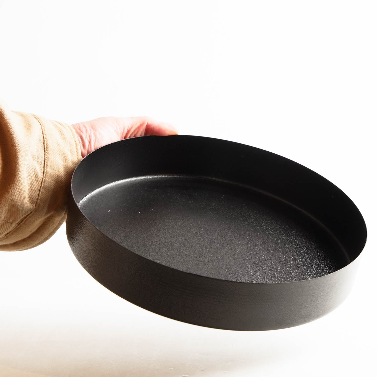 A person's hand holding a black metal tray vase from Hanataba