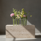 Small bouquet of flowers in clear vases on a stone block against a gray background