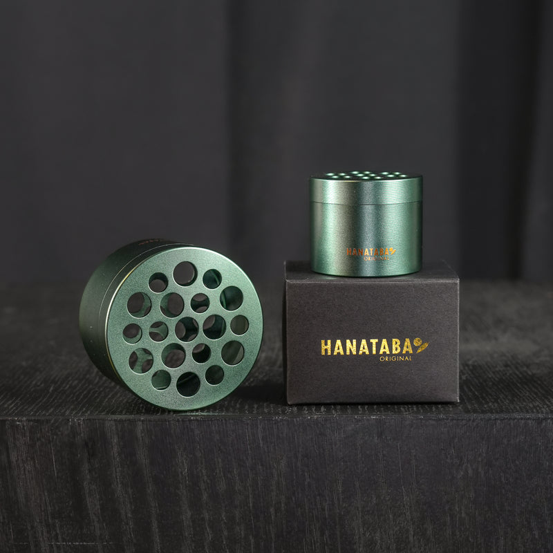 A big and a small Hanataba bouquet twister in ivy green design, in a dark wooden surrounding, displayed on a black packaging box with Hanataba Original branding in golden letters.