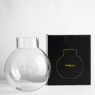 Round empty glass flower bowl with a narrow neck in a white space next to a black Hanataba packaging box