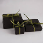 Three gifts wrapped by Hanataba in black paper and golden green ribbon on a white backgroud