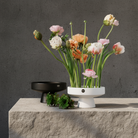 Floral arrangement in a white ceramic ikebana vase vase on a stone surface with a dark gray background