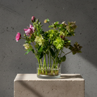 Glass vase with flowers stuck to a 120 mm kenzan ring by hanataba on a concrete block against a gray background