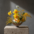 Bouquet of yellow flowers in a decorative vase on a concrete block with a dark background