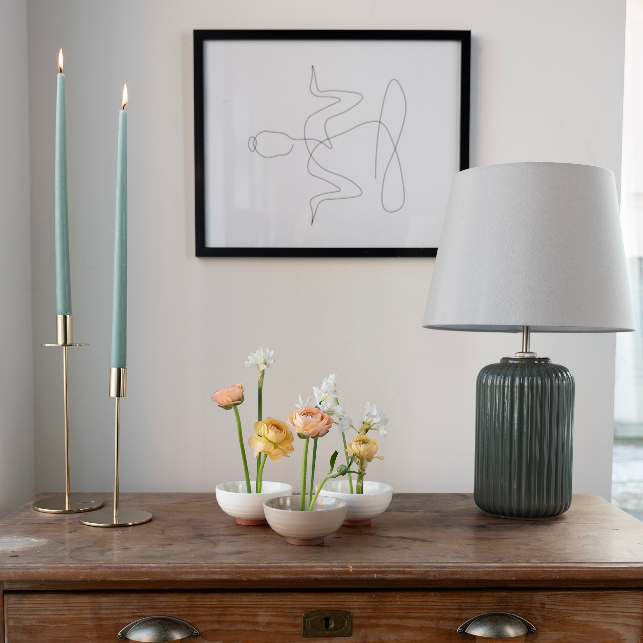 Decorative setup with candles, flowers inside ceramic kenzan 'kobachi' bowls, and a lamp on a wooden surface.