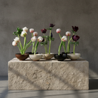 Set of small ceramic kenzan pots with tulips on a stone surface against a gray wall