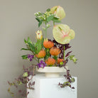 Hanataba kenzan ring 200 mm in a biege marble decor plate containing, Anthurium, Pincushion Protea, Passionflower, Leucadendron, Euphorbia and Tradescantia, placed on a white stand