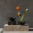 Black bowls and a small arrangement of flowers on a stone platform with a dark background