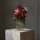 Bouquet of red roses and white baby's breath in a Lisign MILANO vase on a concrete block with a dark background