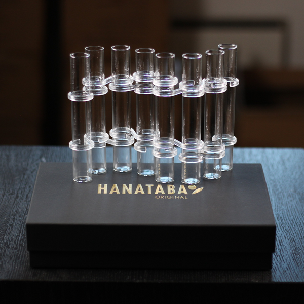 A Hanataba Original Flower Flute set displayed atop a sleek black box with gold branding, featuring a collection of transparent glass tubes designed for creative floral displays.
