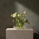 Clear rippled glass vase with flowers on a concrete block against a dark background