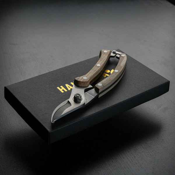 Stylish secateurs with wooden handles on a black box with 'HANATABA' branding in gold, embodying sophisticated flower cutting tools.