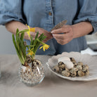 Person arranging flowers in a vase with hanataba waterbubbles and quail eggs on a table