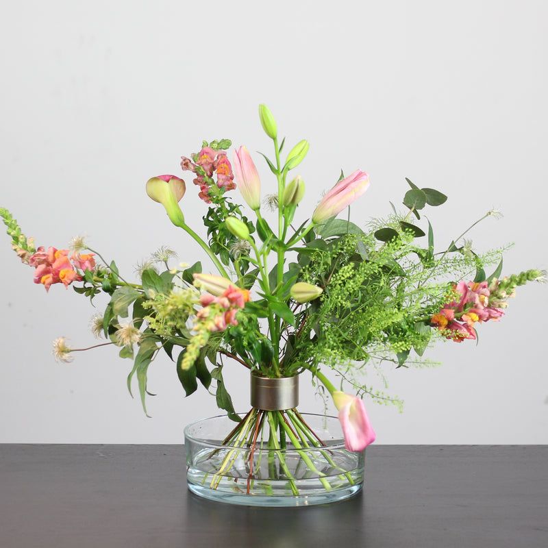 A diverse mix of colorful flowers arranged in a clear bowl vase, held together by a Hanataba Pitch Black Bouquet Twister