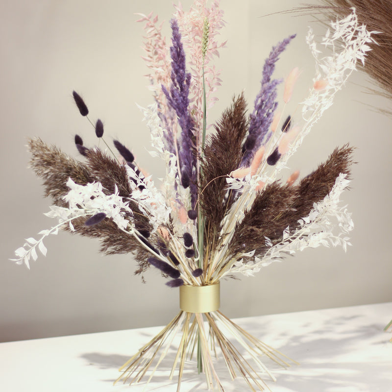 A Hanataba Champagne Gold bouquet with purple, black, and white foliage against a neutral backdrop, showcasing modern elegance.