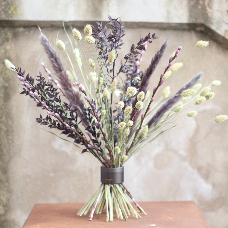 A bouquet of dark purple foliage and light green flowers secured with a Hanataba Pitch Black twister on a wooden surface.